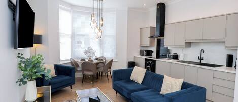 A modern living room with a blue sofa, a glass coffee table, and a flat-screen TV.