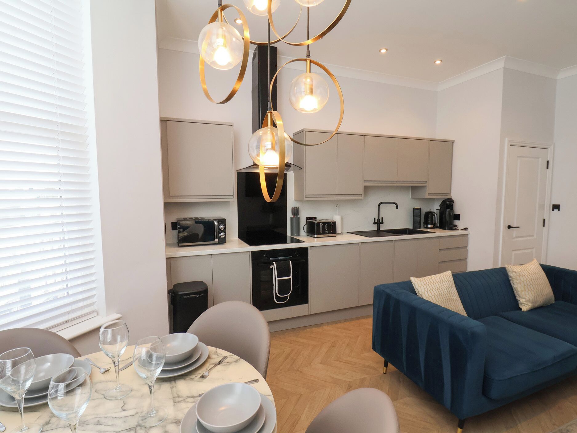 A modern kitchen with a dining area, including a table set for four, a blue sofa, and a unique chandelier.