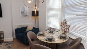 Ein zeitgemäßer Essbereich mit einem runden Tisch, gedeckt für vier Personen, einem blauen Sofa und einem dekorativen Zweig im Fenster.