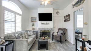 Una sala de estar con sofá, sillón, mesa de centro, chimenea, televisor y ventilador de techo.