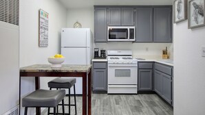 Cocina compacta con refrigerador, microondas, estufa y un pequeño comedor con taburetes.