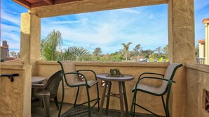 Un balcón con dos sillas y una mesita, con vistas a una zona residencial con árboles y casas.