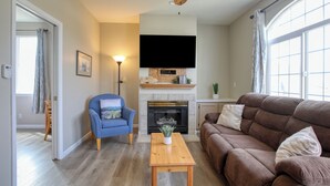 Una sala de estar con chimenea, un sillón azul, un sofá marrón y una mesa de centro de madera.