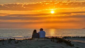 Ein Sonnenuntergang über dem Meer, zwei Personen sitzen am Strand.