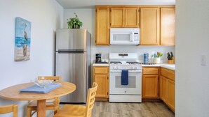 Una cocina compacta con armarios de madera, un refrigerador de acero inoxidable, un microondas y una estufa a gas.