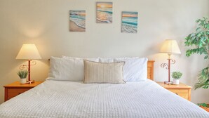Una cama bien hecha con ropa blanca, dos mesitas de noche con lámparas y tres cuadros en la pared.