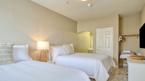 Une chambre d’hôtel avec deux lits, une table de chevet avec une lampe, une commode en bois et une porte avec un porte-serviettes.