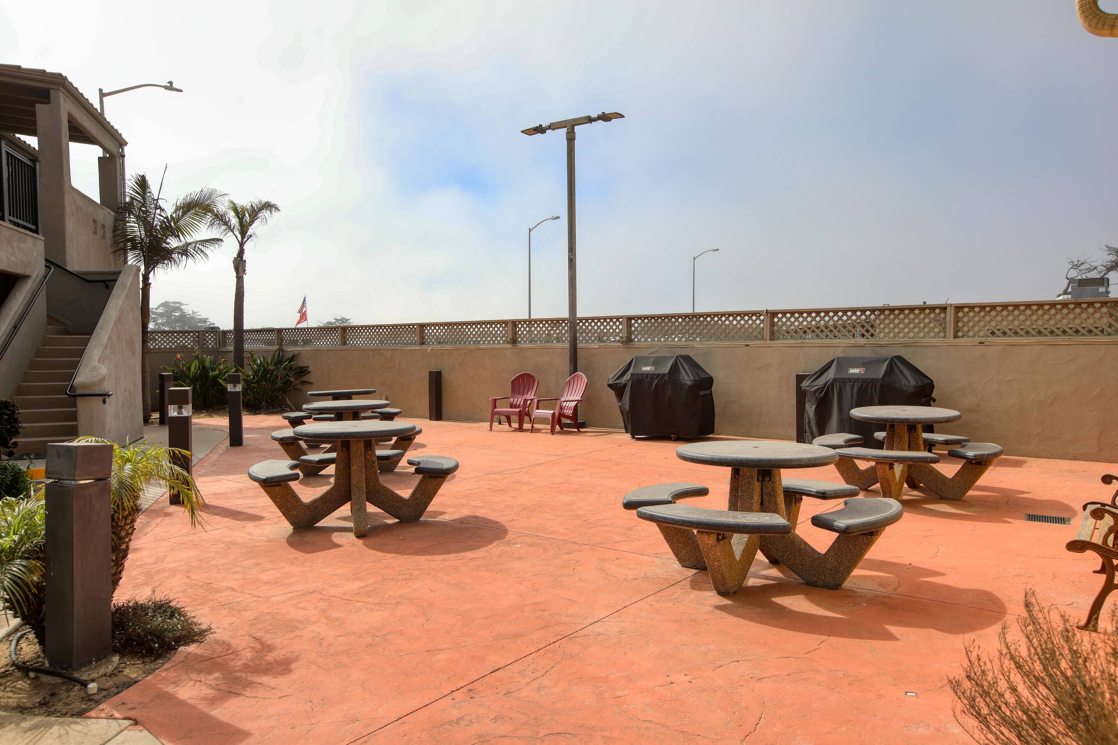 Un espace extérieur aménagé en terrasse, avec des tables et des chaises en pierre, un barbecue et un coin salon abrité.