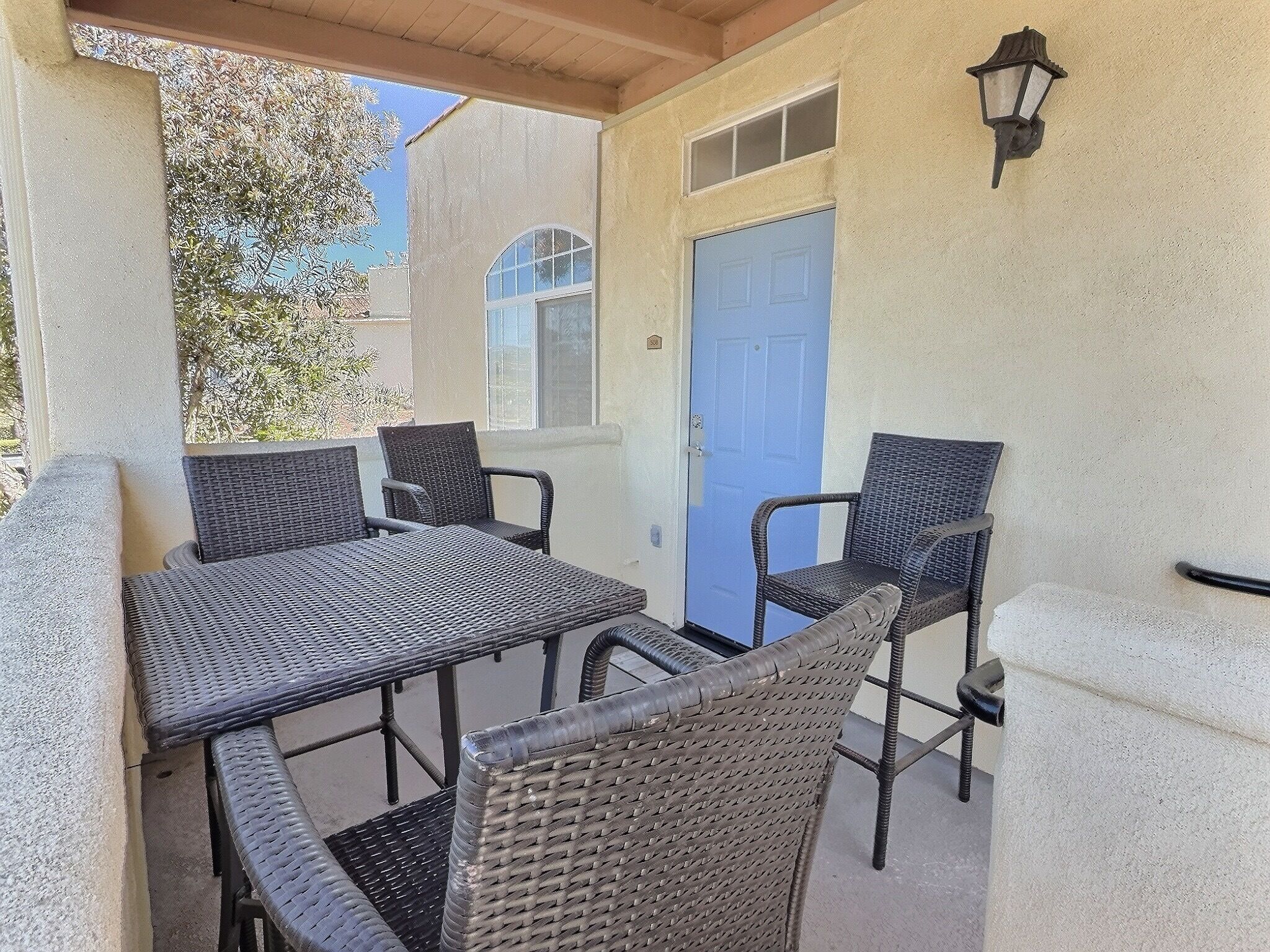 Une terrasse extérieure avec des meubles en osier, une porte bleue et un luminaire fixé au mur.