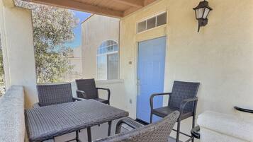 Une terrasse extérieure avec des meubles en osier, une porte bleue et un luminaire fixé au mur.