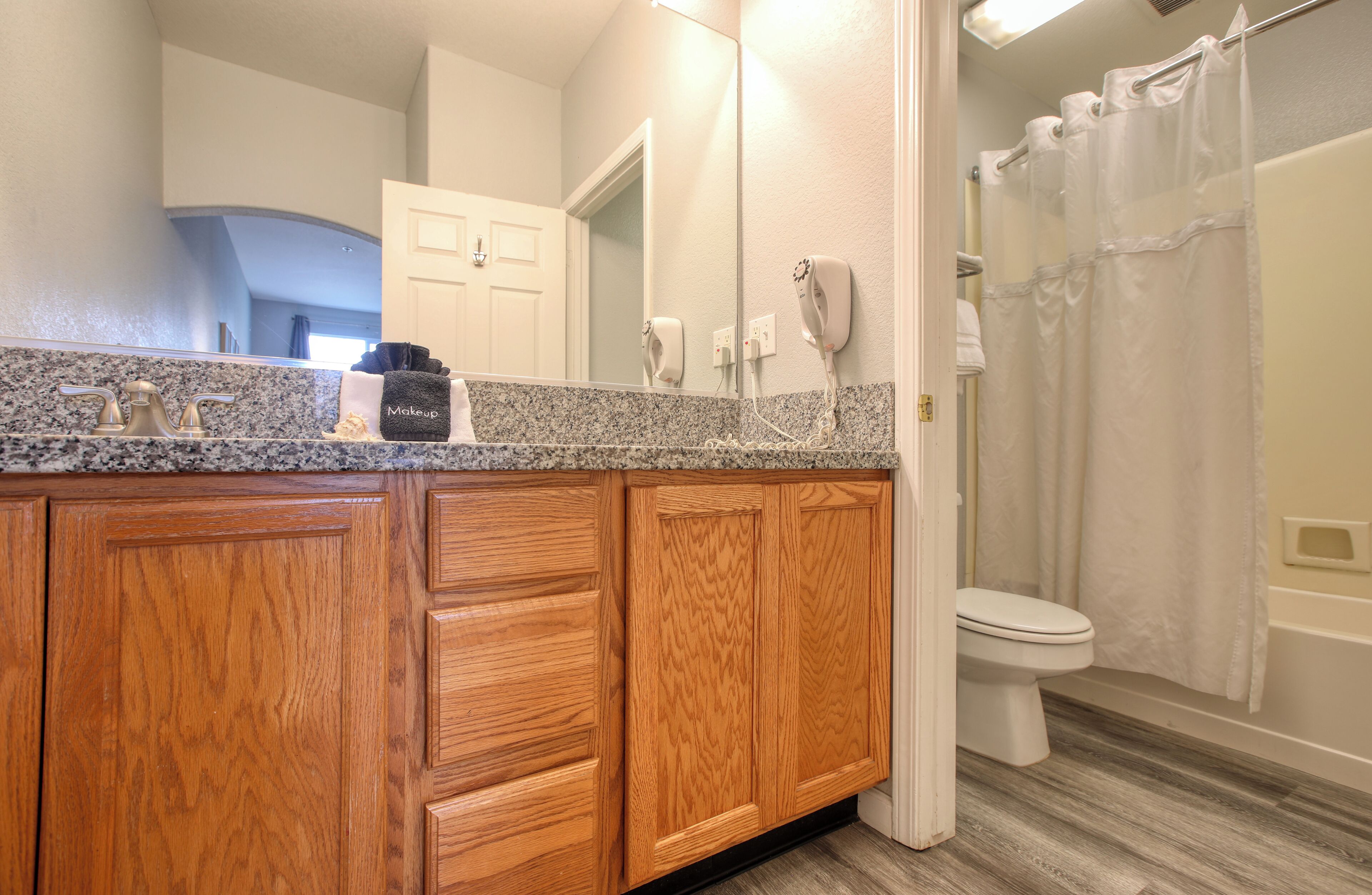 A bathroom with wooden cabinets, a granite countertop, a hairdryer, and a shower curtain.