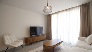 A modern living room with a sofa, armchair, coffee table, TV, and wooden cabinet. - Happy Travel Lily Home Higueron (Fuengirola)