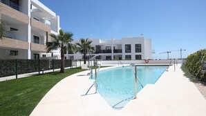 A modern apartment building with a swimming pool, palm trees, and a clear blue sky. - Happy Travel Lily Home Higueron (Fuengirola)