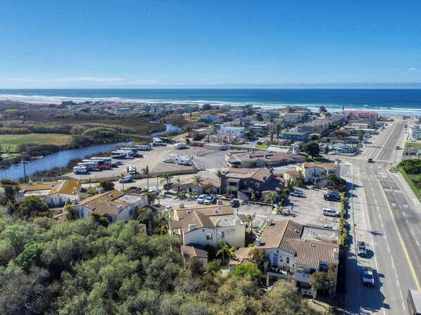 Vue aérienne d’une ville côtière avec un port de plaisance, des immeubles résidentiels et une route menant à la plage.