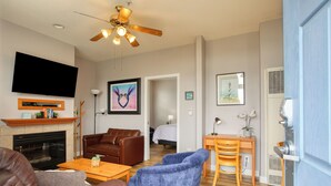 Un salon avec une cheminée, un canapé en cuir, un fauteuil bleu, une table basse en bois et un ventilateur de plafond.