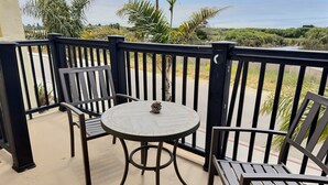 Un balcon avec une table ronde et deux chaises, donnant sur un paysage composé d’arbres et d’une route.