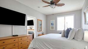 Une chambre à coucher comprenant un lit, une commode, un téléviseur et un ventilateur de plafond.
