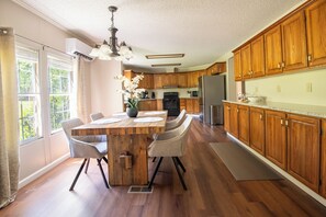Een keuken met houten kastjes, een centraal eiland met stoelen, een koelkast en een raam met gordijnen.