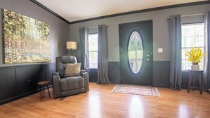 Un salon spacieux avec un grand canapé de couleur sombre, une petite table d’appoint, un lampadaire et un grand tableau abstrait accroché au mur.
