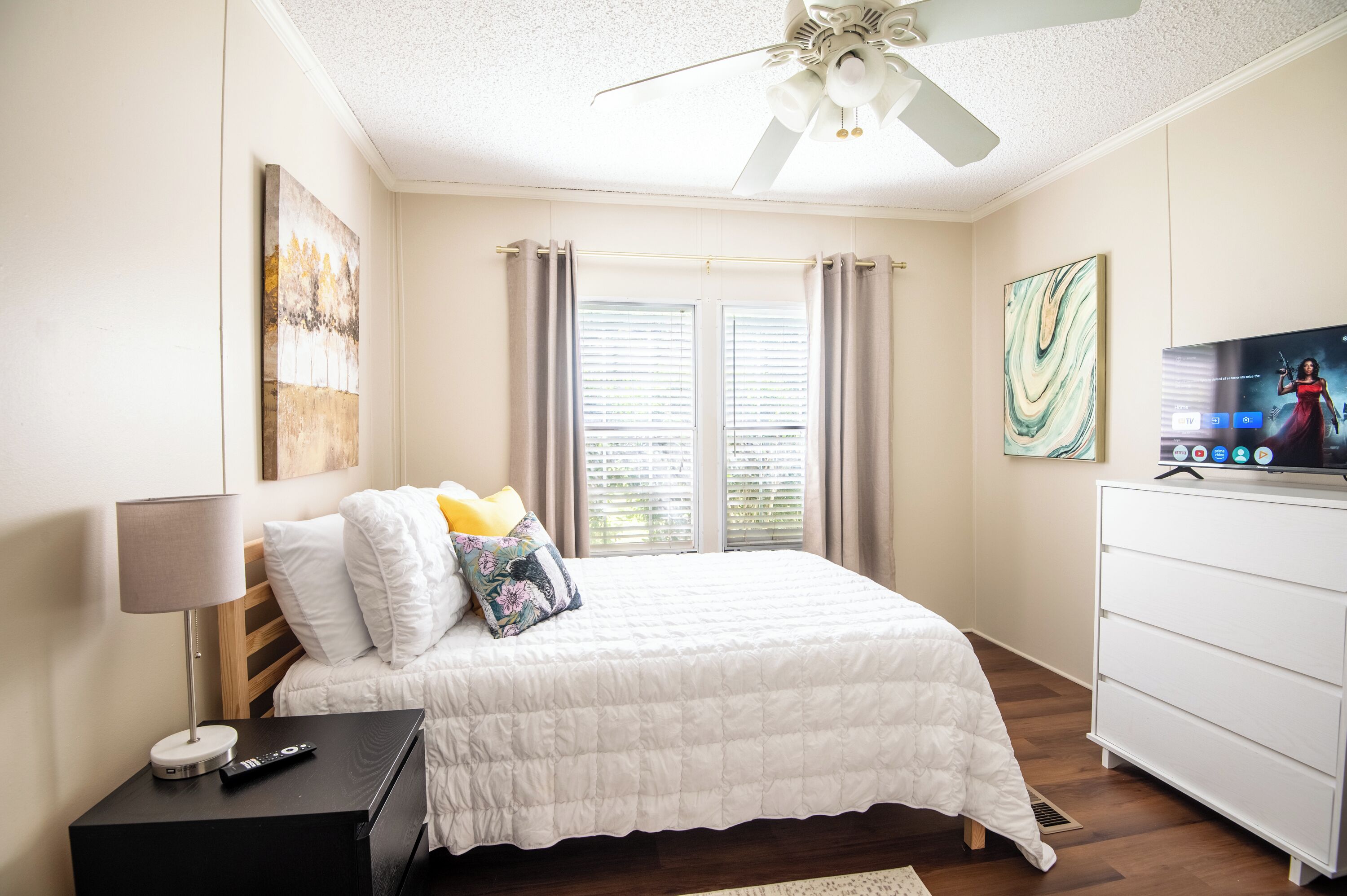 A neatly arranged bedroom with a bed, bedside table, lamp, and a TV on a dresser.