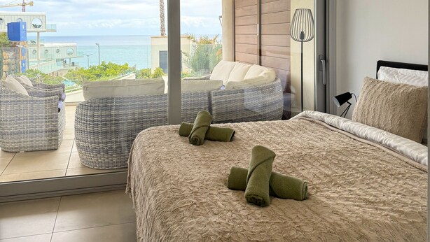 A bedroom with a large bed, a view of the ocean, and a balcony with wicker furniture. - Happy Travel Panoramica (Fuengirola)