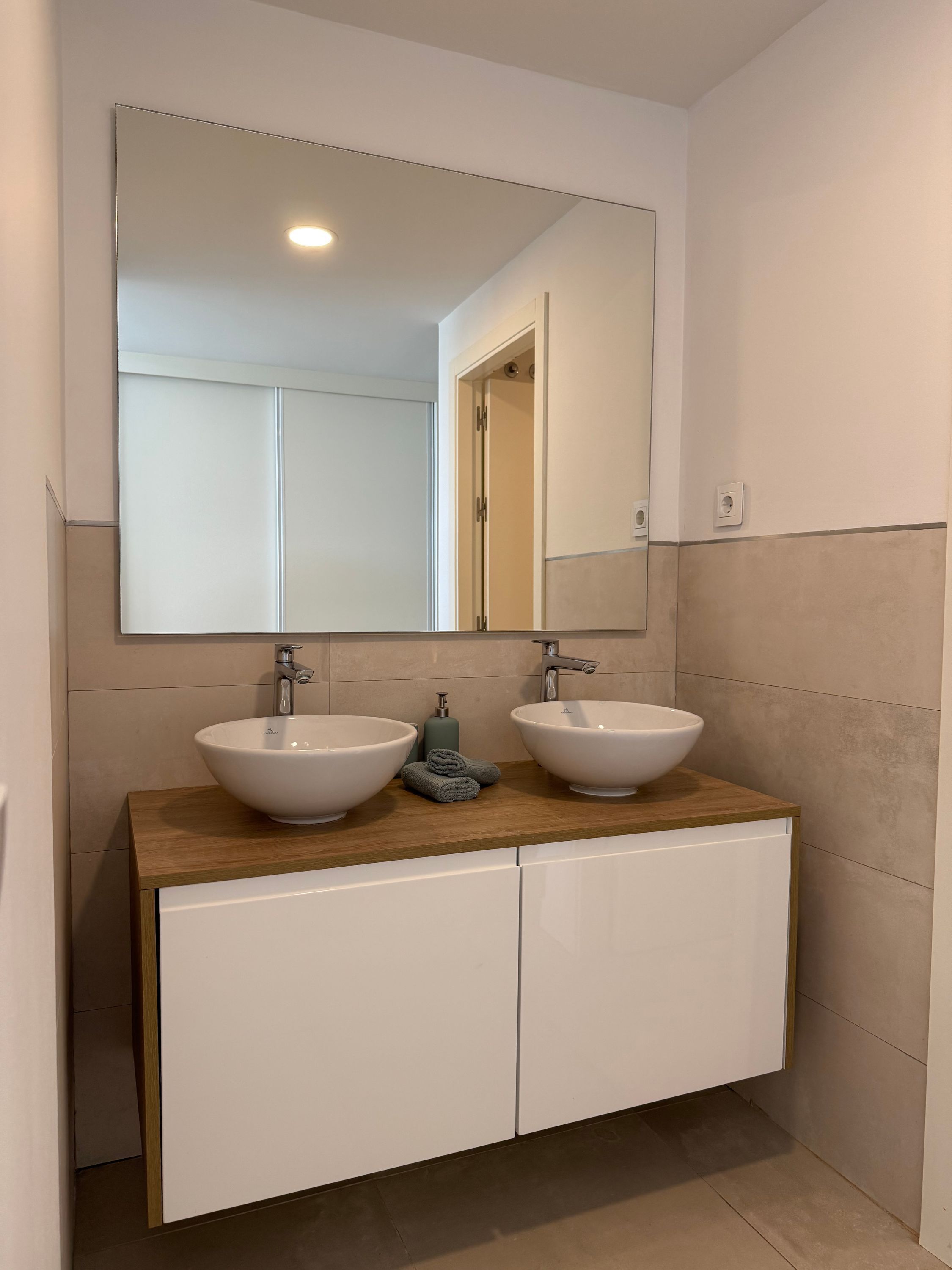 A bathroom with two white sinks, a large mirror, and a wooden countertop.