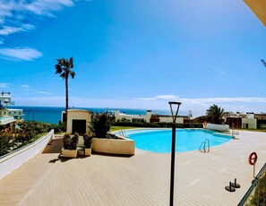 A pool area with a clear view of the ocean, surrounded by modern buildings and palm trees. - Happy Travel Panoramica (Fuengirola)
