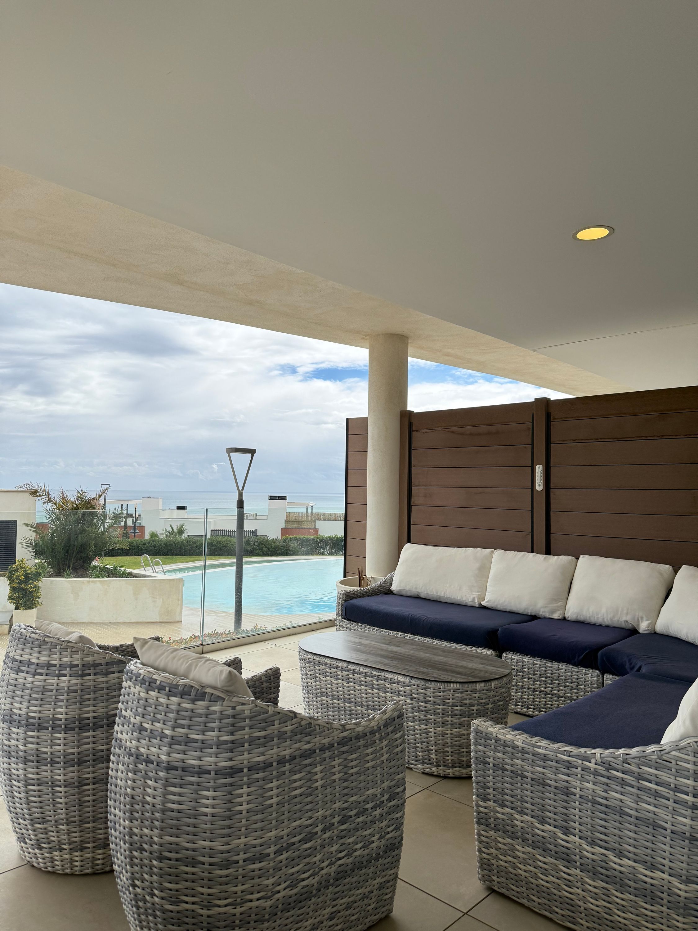 A modern outdoor lounge area with a pool view, wicker furniture, and a large sofa with cushions.