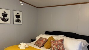 A neatly made bed with a yellow blanket, white pillows, and a black headboard. Two framed artworks are hung on the wall above the bed.