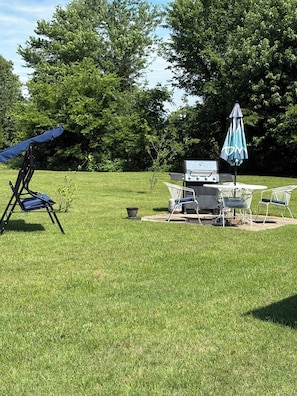 A backyard with a grill, outdoor furniture, and a swing chair.