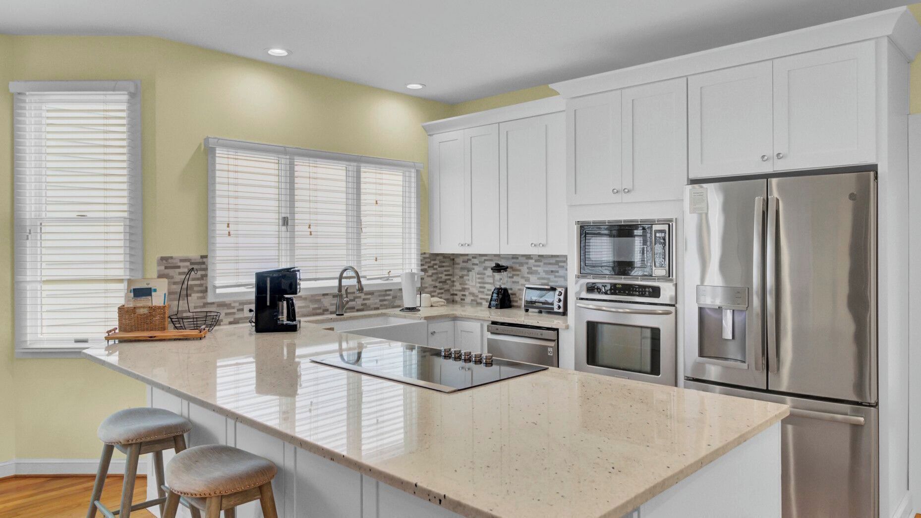 A modern kitchen with white cabinets, a stainless steel refrigerator, an oven, and a coffee maker.