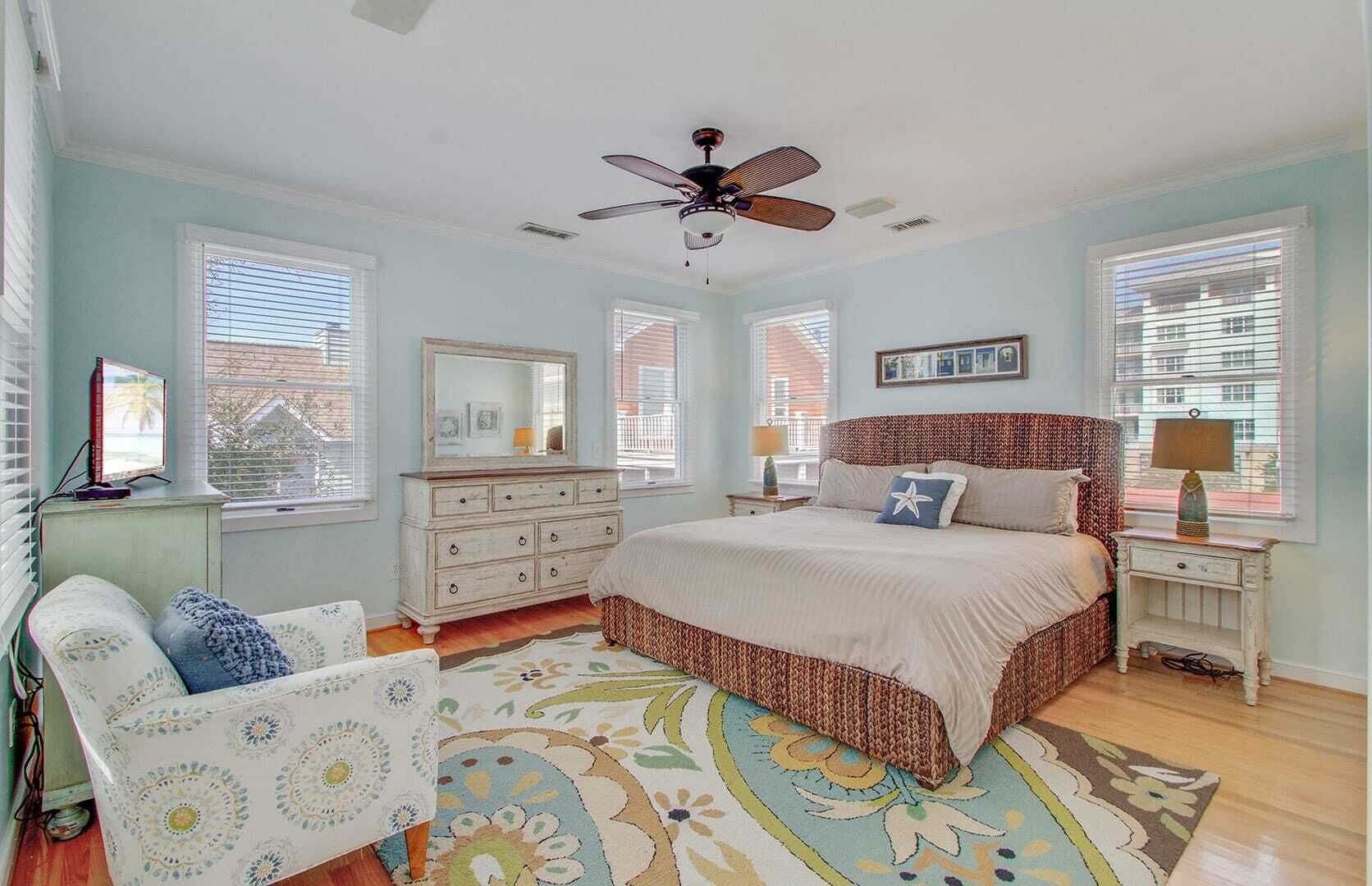 Une chambre à coucher comprenant un lit, une commode, des tables de chevet, un ventilateur de plafond et un tapis à motifs.