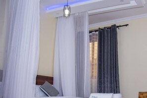 Un dormitorio con cama, cortinas blancas, una cortina oscura y una lámpara colgante.
