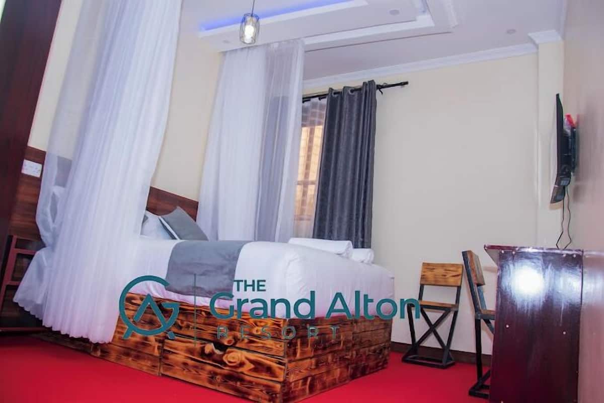 Una habitación de hotel con estructura de cama de madera, ropa de cama blanca, alfombra roja, escritorio de madera y televisor en la pared.
