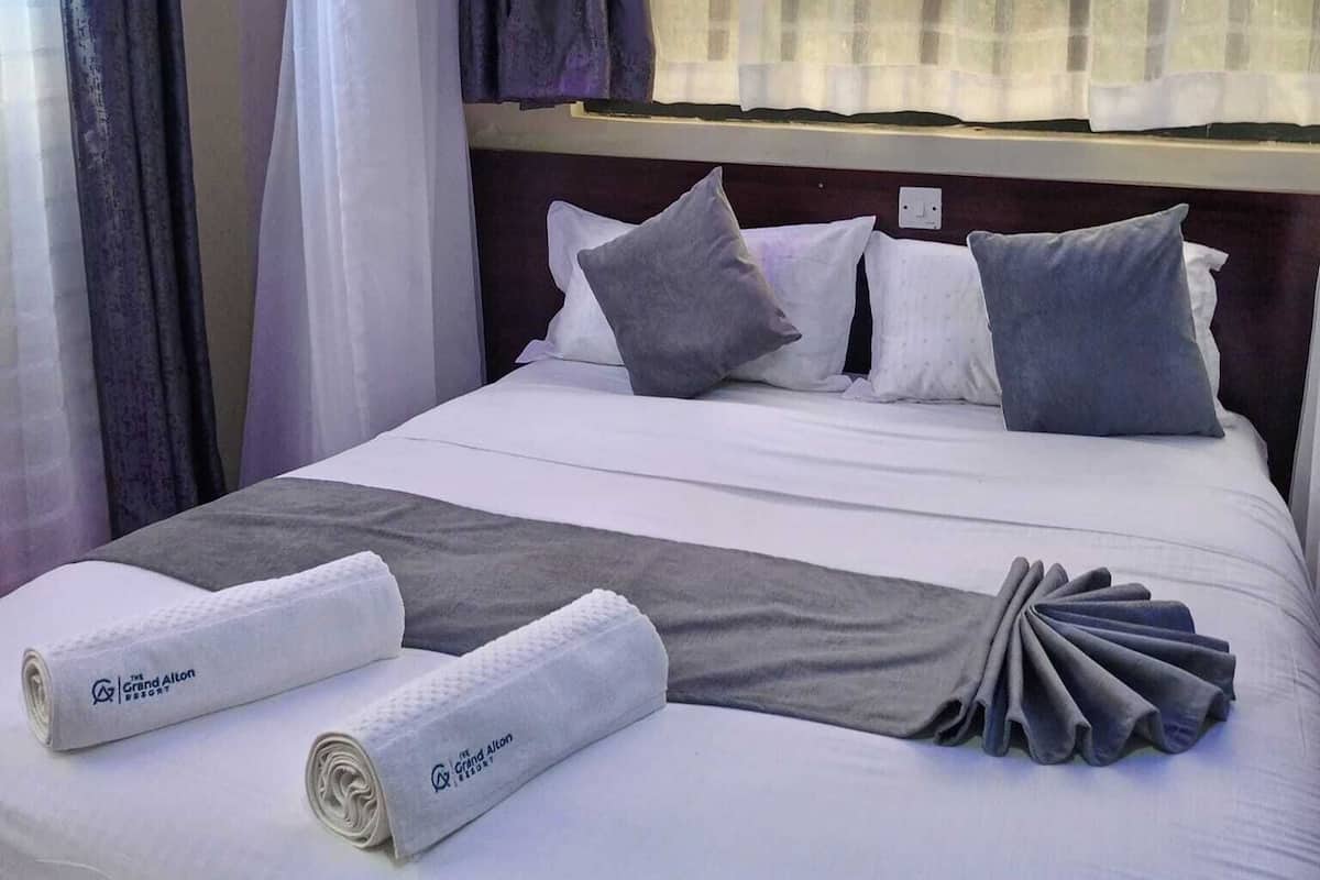 Una habitación de hotel con una cama bien hecha, cabecera y una ventana con cortinas traslúcidas.