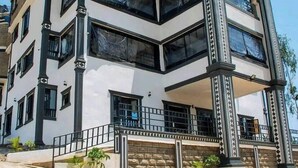 A corner building with a white facade, black trim, and multiple windows. - The Grand Alton resort (Kisumu)