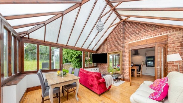 A spacious room with a wooden dining table, a red sofa, and a white sofa. There is a television and a lamp in the room. - Spacious rural escape for groups & families (Shropshire)