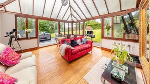 A conservatory with a red sofa, a telescope, and a glass table. - Spacious rural escape for groups & families (Shropshire)