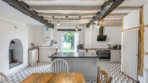 A rustic kitchen with a wooden table and chairs, white cabinets, and a patterned floor. - Spacious rural escape for groups & families (Shropshire)