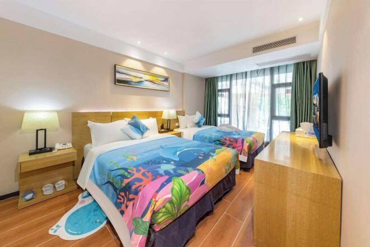 A hotel room with two beds, a desk, a TV, and a window with curtains.