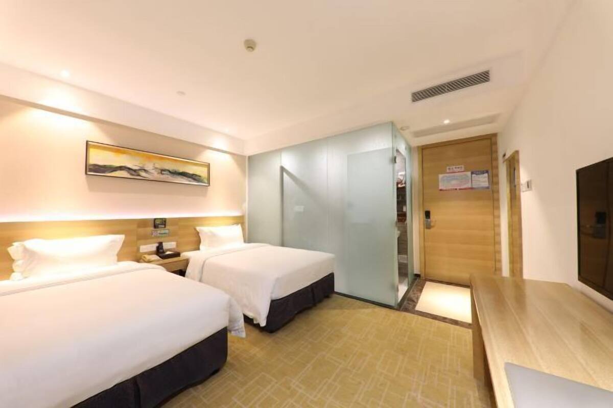 A hotel room with two beds, a wooden desk, a painting on the wall, and a door with a sign.