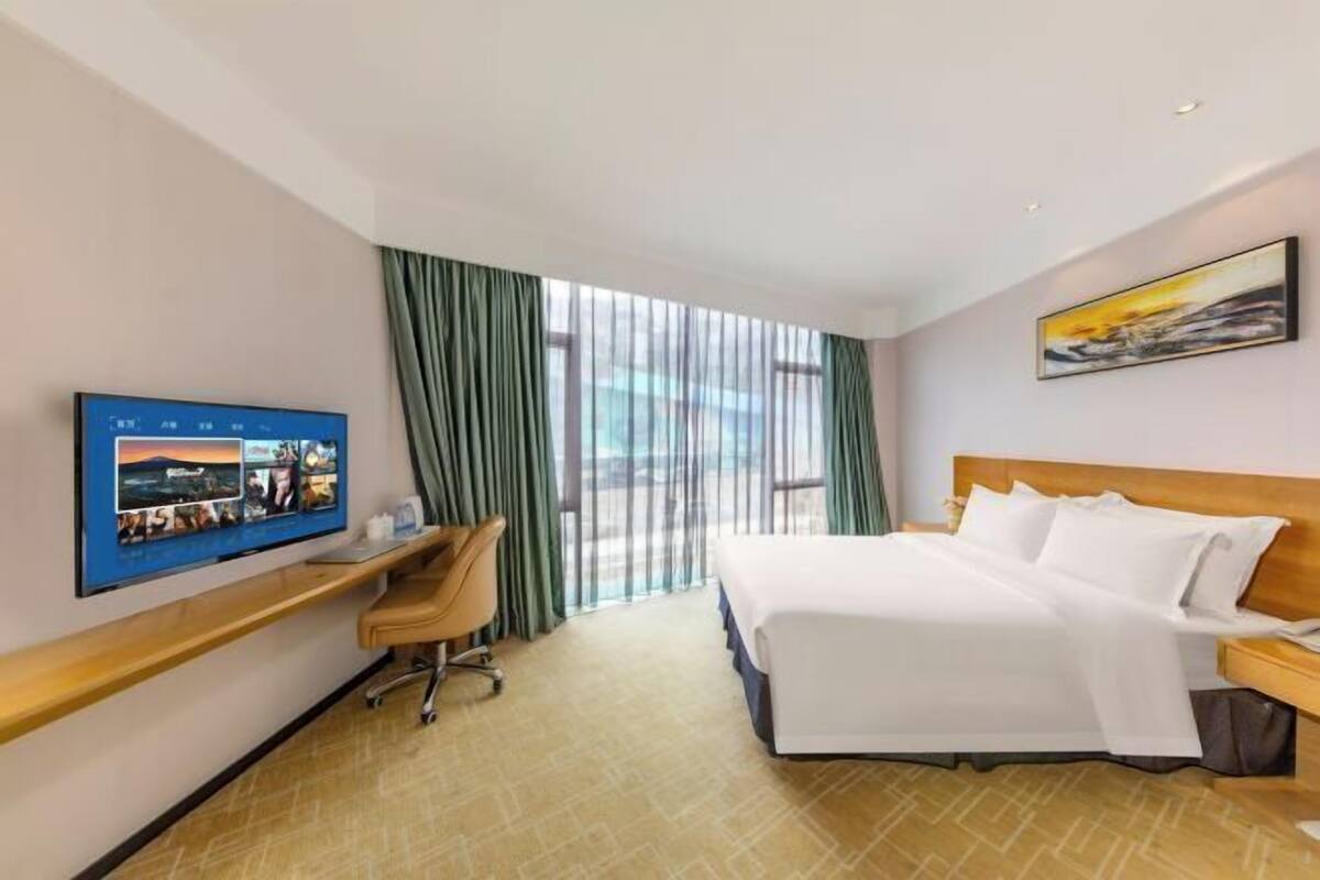 A hotel room with a bed, a desk, a chair, a TV, and a window with curtains.
