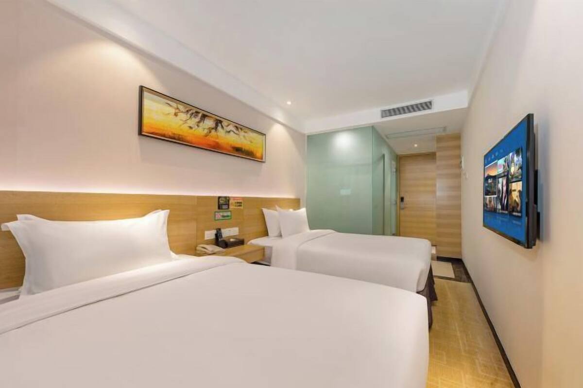 A hotel room with two beds, a painting on the wall, and a television mounted on the wall.