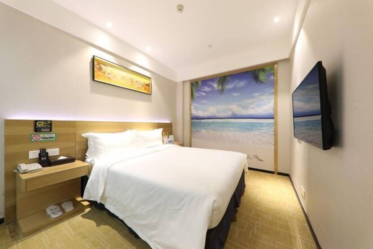 A hotel room with a bed, nightstand, and a painting of a beach scene.