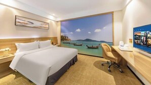 Une chambre d’hôtel équipée d’un lit, d’un bureau, d’une chaise et d’une grande fenêtre donnant sur un paysage où l’on peut admirer des bateaux sur l’eau.