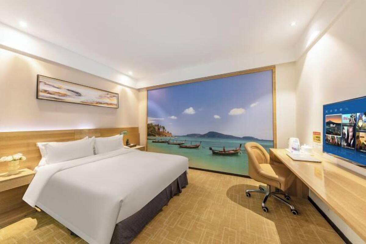 A hotel room with a bed, desk, chair, and a large window with a view of boats on water.