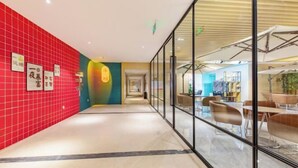 Un couloir avec un mur recouvert de carreaux rouges, des cloisons en verre et des meubles modernes.