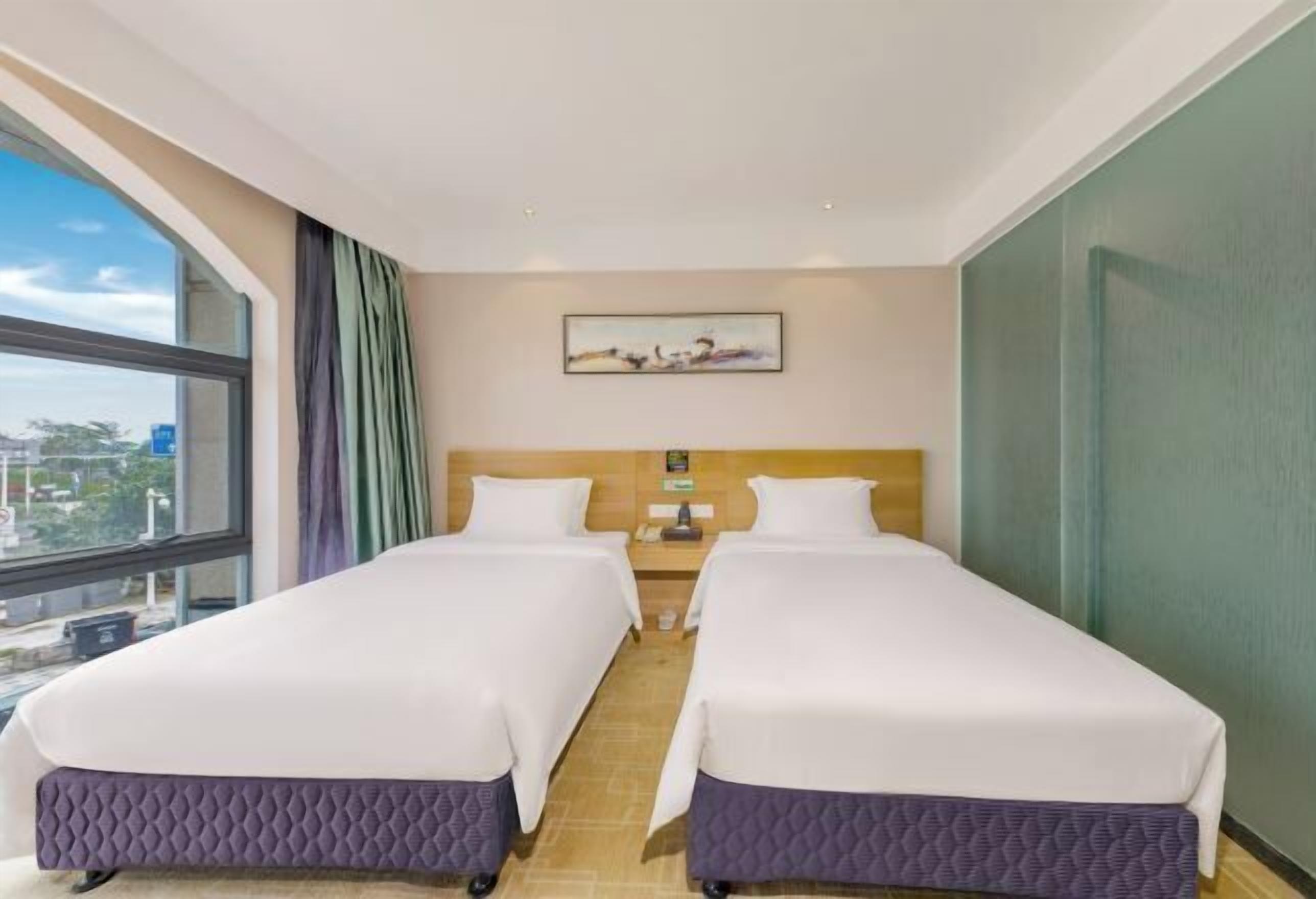 A hotel room with two beds, a window with curtains, a painting on the wall, and a nightstand with a lamp.