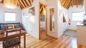 Een knus vertrek met houten balken, een zithoek met tafel en stoelen, een keuken met spoelbak en aanrecht, en een badkamer met toilet en wastafel.