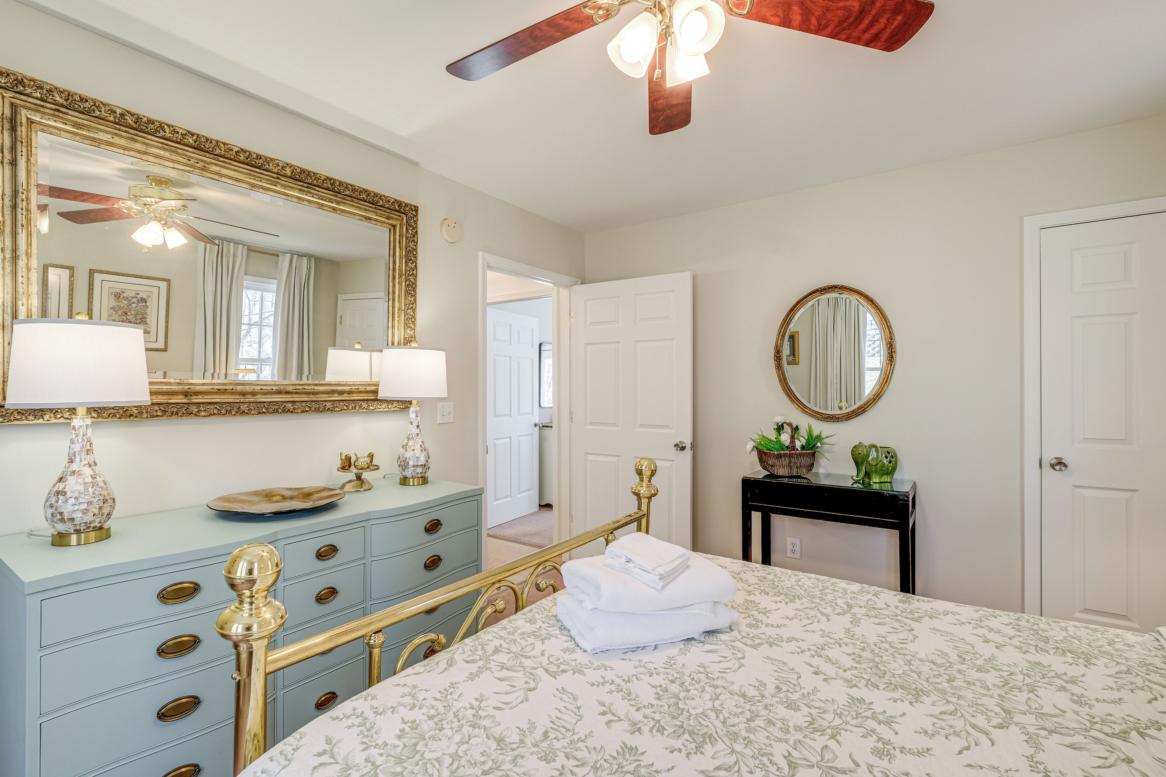 A bedroom with a bed, a dresser, a mirror, and a ceiling fan.